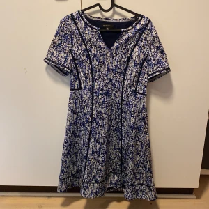Blå och vit klänning från Banana Republic - Säljer en superfin blå och vit klänning från Banana Republic. Den har ett unikt mönster och korta ärmar. Perfekt för både vardag och fest! Klänningen har en v-ringad hals och är i mycket bra skick.