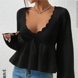 Svart stickad tröja med knytband - Snygg svart stickad tröja med v-ringad design och knytband i midjan. Den har långa ärmar och en ribbad struktur som ger en skön passform. 