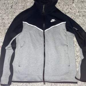 Säljer en snygg grå och svart hoodie från Nike. Den har en dragkedja framtill och en huva för extra skydd. Perfekt för höst och vår, med en sportig look. Jackan är i mycket bra skick och har långa ärmar. Perfekt för träning eller vardagsbruk! Om ni har fråga så kan ni skriva och pris kan diskutera.