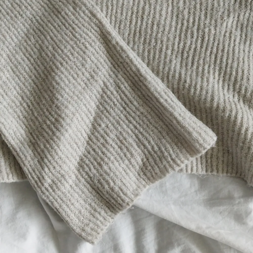  beige off-shoulder tröja i ribbat material. Perfekt för kyliga dagar med sin långa ärmar och bekväma passform. Enkelt att matcha med jeans eller kjol för en avslappnad look.. Tröjor & Koftor.