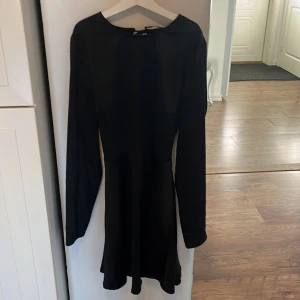 Svart långärmad klänning med snörning - Snygg svart klänning i mycket bra skick. Den har långa ärmar och en elegant snörning i ryggen som ger en unik touch. Perfekt för höst- och vinterfester eller en stilren vardagslook. Materialet känns mjukt och bekvämt mot huden.