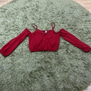 Röd offshoulder topp från H&M Divided - Snygg röd offshoulder topp från H&M Divided i storlek XS. Toppen har långa ärmar och smala axelband, vilket ger en trendig look. Perfekt för festliga tillfällen eller en utekväll. Den är i bra skick och redo att bäras av någon som vill sticka ut!