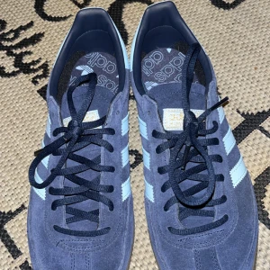 Blå Adidas Spezial sneakers - Säljer ett par snygga Adidas Spezial sneakers i blå mocka med ljusblå ränder. De har en klassisk design med snörning och en bekväm gummisula. Perfekta för både vardag och fest! Skorna är i mycket bra skick och redo för nya äventyr.