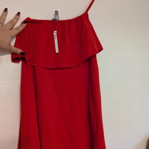 Röd klänning från ASOS - Superfin röd klänning från ASOS i storlek S. Den är axelbandslös med en volangdetalj upptill. Tillverkad i 100% bomull, vilket gör den både bekväm och sval.ny