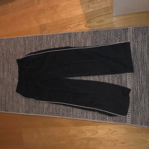 Svarta byxor med vita detaljer - Säljer ett par svarta byxor med vita ränder längs sidorna. De har en loose passform och är perfekta för en avslappnad stil. Byxorna är i bra skick och passar till vardags eller gymmet. Perfekta för höst och vår!