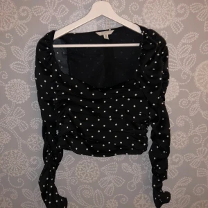 Svart prickig topp - Säljer en superfin svart topp med vita prickar. Den har långa ärmar och en snygg rynkad detalj framtill som ger en smickrande passform. Perfekt för både vardag och fest! 🖤