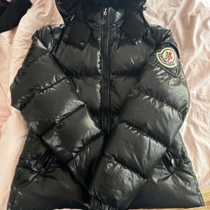 Svart pufferjacka från Moncler - Säljer en snygg svart pufferjacka från Moncler i mycket bra skick. Den saknar tyvärr cartoon loggan men i övrigt är den hur fin som helst! Den är köpt på Vestiaire Collective och är 100% äkta! Inspektions tag medföljer🌸storlek 4 men väldigt liten i storleken så passar mer som en M, perfekt för dig som vill ha den oversized! Säljs då den inte kommer att komma till användning🫶🏽