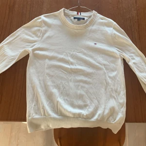 Vit tröja från Tommy Hilfiger - Säljer en stilren vit tröja från Tommy Hilfiger i mycket bra skick. Tröjan är långärmad och har en liten logga på bröstet. Den är gjord i mjukt bomullsmaterial och har ribbade muddar vid ärmslut och nederkant. Perfekt för både vår och höst!
