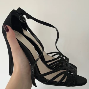 Svarta sandaler med klack - Snygga svarta 00s klackar från No. 1 Jenny Packham. Öppen tå och sluten klack! Fina stenar på de främre banden och 10cm höga. Köpta second hand!