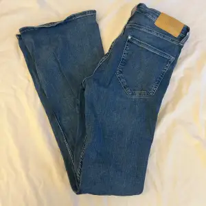 Säljer ett par snygga blå flare jeans i storlek 36. De har en hög midja som ger en skön passform och är perfekta för både vardag och fest. Materialet är denim, vilket gör dem hållbara och bekväma. Passar perfekt till en t-shirt eller en snygg blus!