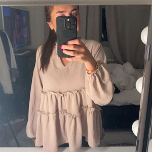 Beige blus med volanger - Säljer en superfin beige blus med volanger. Den har långa ärmar och en v-ringad hals. Perfekt för både vardag och festliga tillfällen. Blusen är i ett mjukt och bekvämt material.