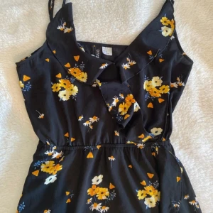 Svart blommig klänning från H&M - Säljer en superfin svart klänning från H&M Divided med blommigt mönster i gult och vitt. Klänningen har en söt krage och är ärmlös, perfekt för sommardagar. Den har en elastisk midja för en bekväm passform. Perfekt för både vardag och fest! Är i väldigt bra skick!🌻