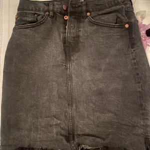 Svart jeanskjol - Snygg svart jeanskjol i kort modell med rå kant. Perfekt för en casual look eller att klä upp med en snygg topp. Kjolen har klassiska fem fickor och knappar fram. Passar perfekt till både vår och sommar!