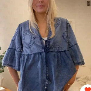 Blå tröja med broderade detaljer - Säljer en vacker blå tröja med broderade detaljer och v-ringning. Tröjan har korta ärmar och ett knytband i midjan för en fin passform. Perfekt för vår och sommar!