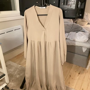 Beige långklänning med v-ringning - Säljer en superfin beige långklänning med v-ringad hals. Klänningen har långa ärmar och en lös passform som ger en avslappnad look. 