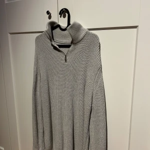 Grå stickad tröja från Zara - Säljer en stilren grå stickad tröja från Zara med dragkedja och hög krage. Perfekt för kyliga dagar och ger en avslappnad look. Tröjan har långa ärmar och en mjuk textur.