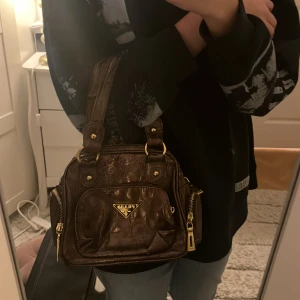 Brun vintage väska - Snygg brun handväska med gulddetaljer. Väskan har flera dragkedjor och en praktisk design med dubbla handtag. Perfekt för att bära dina dagliga nödvändigheter med stil.
