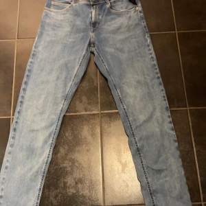 Blå jeans från Replay - Snygga ljusblå jeans från Replay med klassisk femficksdesign. De har en knappgylf och är tillverkade i ett slitstarkt denimtyg. Perfekta för en avslappnad stil.