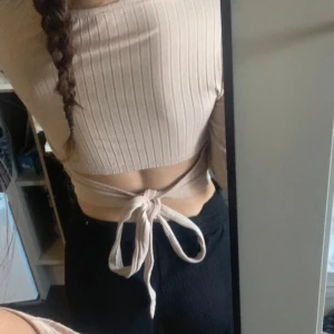 Beige ribbad croppad topp - Säljer en beige ribbad croppad topp med långa ärmar och knytning i ryggen. Perfekt för en stilren och bekväm look.