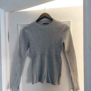 Grå ribbad tröja från Crocker - Säljer en stilren grå ribbad tröja från Crocker. Tröjan har långa ärmar och en rund halsringning, perfekt för kyligare dagar. Passar bra till både jeans och kjol.