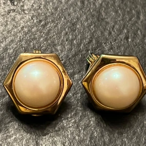 Vintage Guldörhängen med pärlor från Monet - Eleganta vintage guldörhängen från Monet med en stor, rund pärla i mitten. Designen är sexkantig vilket ger en unik och stilren look. Perfekta för att ge en touch av glamour till din outfit.