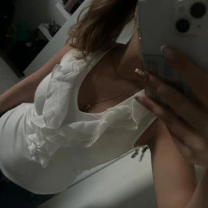 Vit ärmlös blus med volangdetaljer - Snygg vit blus med volangdetaljer framtill. Den är ärmlös 