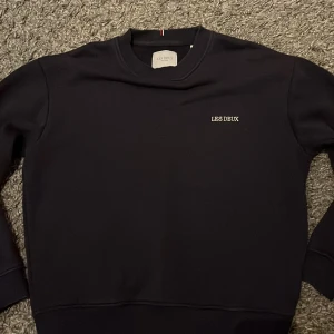 Mörkblå sweatshirt från Les Deux - Snygg mörkblå sweatshirt från Les Deux med diskret logga på bröstet. Tröjan har en klassisk rund halsringning och ribbade muddar vid ärmslut och nederkant. Perfekt för en stilren look. Skriv gärna vid fler frågor. Priset kan diskuteras.