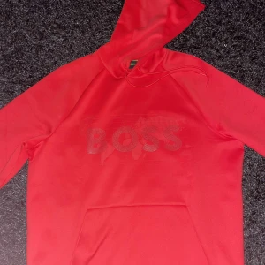 Röd dress från Hogo Boss - Snygg röd dress från Boss med ett diskret mönster och logga på bröstet. Tröjan har en praktisk magficka och en bekväm huva. Perfekt för en avslappnad stil. Kvitto finns