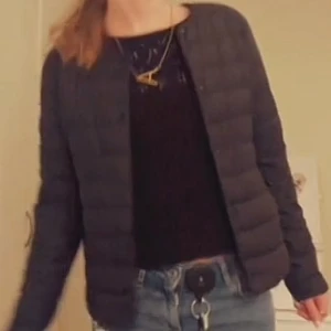 Svart pufferjacka uniqlo - Snygg svart pufferjacka med långärmad design. Perfekt för kyligare dagar med sin quiltade stil. Enkel och stilren utan krage, vilket gör den lätt att matcha med olika outfits.