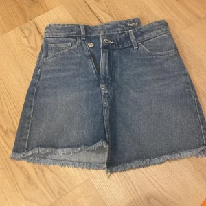 Jeanskjol från H&M - Snygg jeanskjol från H&M i klassisk blå denim. Kjolen har en rå kant nertill och praktiska fickor både fram och bak. Perfekt för en avslappnad stil.