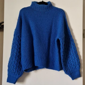 Blå stickad tröja från Samsa Collection - Säljer en snygg blå stickad tröja från Samsa Collection. Tröjan har en hög krage och långa ärmar med ett unikt stickat mönster. Perfekt för kyliga dagar!