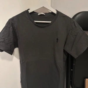 Grå t-shirt från Saint Laurent - Snygg grå t-shirt från Saint Laurent med en liten broderad logga på bröstet. Perfekt för en stilren och avslappnad look.