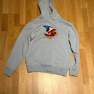 Ljusblå hoodie med Disney-motiv - Säljer en ljusblå hoodie med ett coolt Disney-motiv på framsidan. Tröjan har en stor ficka framtill och en bekväm huva. Perfekt för alla Disney-fans! 💙
