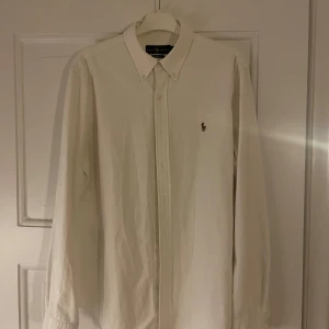 Vit skjorta från Ralph Lauren - Klassisk vit skjorta från Ralph Lauren i storlek L. Skjortan har långa ärmar och en broderad logotyp på bröstet. Perfekt för en stilren look.