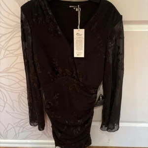 Svart glittrig klänning från Gina Tricot - Snygg svart klänning från Gina Tricot i storlek XS. Klänningen har långa ärmar och är täckt med glittriga paljetter som ger en festlig look. Den har en omlott-design och en kort längd som passar perfekt för en utekväll. Aldrig använd, ba testad!