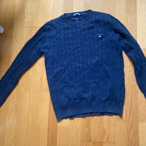 Mörkblå kabelstickad tröja från GANT - Säljer en snygg mörkblå stickad tröja från GANT med kabelstickat mönster. Nypris 1300kr, mitt pris 300kr