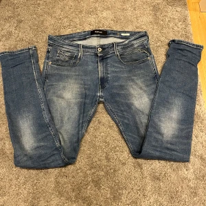 Replay Anbass jeans Blåa - Snygga blå jeans från Replay, modell Anbass. De har en klassisk femficksdesign med subtila slitningar för en trendig look. Perfekta för en avslappnad stil. Byxorna är i mycket bra skick, men har en liten defekt.