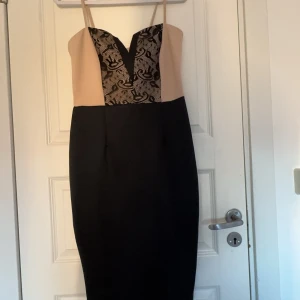 Beige och svart klänning från AX Paris - Elegant klänning från AX Paris i beige och svart med smala axelband och v-ringad spetsdetalj framtill. Perfekt för en stilren look.