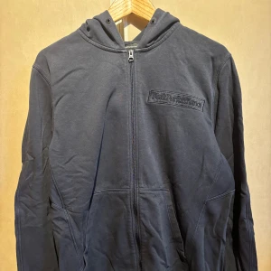 Mörkblå hoodie från Peak Performance - Säljer en snygg mörkblå hoodie från Peak Performance med dragkedja och broderad logga på bröstet. Perfekt för kyliga dagar med sin bekväma passform och huva. Storlek XL. 