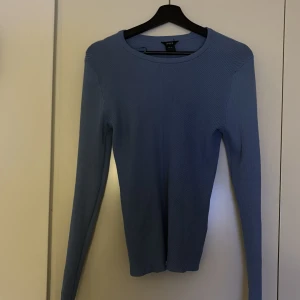 Blå ribbad tröja från Lindex - Säljer en stilren blå ribbad tröja från Lindex. Tröjan har en klassisk rund halsringning och långa ärmar, perfekt för lager-på-lager under kyligare dagar. Passar bra till både jeans och kjol. 🌀