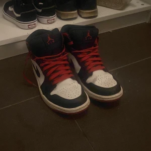 Nike Air Jordan 1 mid gym red black toe - Snygga Nike Air Jordans i svart, vitt och rött med röda snören. Perfekta för dig som vill ha en klassisk sneaker med en sportig touch. Skorna har en hög modell med ikonisk logga på plösen.