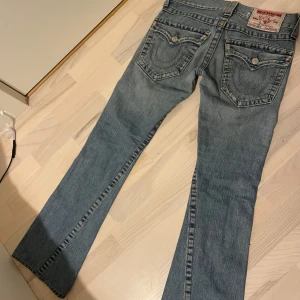 Blå jeans från True Religion - Snygga blå jeans från True Religion med klassisk femficksdesign och kontrastsömmar. De har en knappgylf och märkeslogga på baksidan. Perfekta för en avslappnad stil.