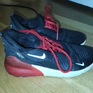 Svarta Nike Air Max med röda detaljer - Säljer ett par svarta Nike Air Max med röda snören och detaljer. Skorna har en vit sula och är perfekta för en sportig look. De är bekväma och stilrena, idealiska för vardagsbruk.