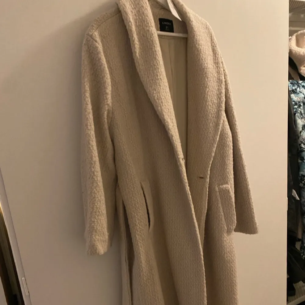 Supersnygg beige Långkappa ifrån Lindex, Storlek L och aldrig använd (lapp kvar) original pris 1499, rabattpris 599, men jag säljer för 400. Bild på en lös knapp. Takit.