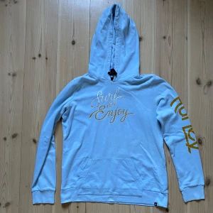 Blå hoodie från Hurley - Säljer en blå hoodie från Hurley med texten 'Surf & Enjoy' i gult på bröstet och ’Hurley’ på ärmen. Den är en tunn hoodie så passar bäst till sommar eller när man är på stranden. Bra skick förutom ett litet hål på framsidan, syns i bild 3 och 4. Står att den är storlek M men skulle säga att den passar mer som S. 