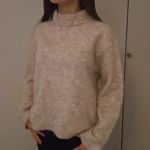 Beige stickad tröja - Mysig beige stickad tröja med hög krage och långa ärmar. Perfekt för kyliga dagar och ger en avslappnad look. Tröjan har ribbstickade muddar vid ärmslut och nederkant.