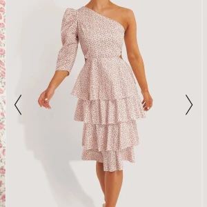 Blommig oneshoulder klänning - Charmig oneshoulder klänning med blommigt mönster i rosa och vitt. Klänningen har en volangdesign med flera lager och trekvartsärm på ena sidan. Perfekt för en somrig look. Kolla gärna in det andra jag säljer!💘