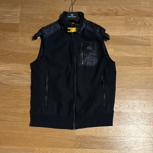 Svart dunväst från Parajumpers - Säljer en stilren svart dunväst från Parajumpers med dragkedja och praktiska fickor. Västen har en quiltad baksida och en liten bröstficka med dragkedja. Perfekt nu till våren. Skick:10/10 (använd en gång). Priset går att diskutera!