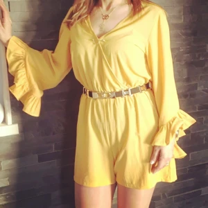 Gul/senapgul Playsuit  med volangärmar - Snygg gul /senapsgul playsuit från New Look med volangdetaljer på ärmarna. Playsuit har en v-ringad design och ett elastiskt band i midjan för en bekväm passform. Perfekt för att lysa upp garderoben! Använd bara en gång!