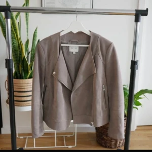 Grå mockajacka från Dagmar - Snygg beige mockajacka från Dagmar i 100% koskinn. Jackan har en stilren design med dragkedja och en modern look. Perfekt för att ge din outfit en extra touch.